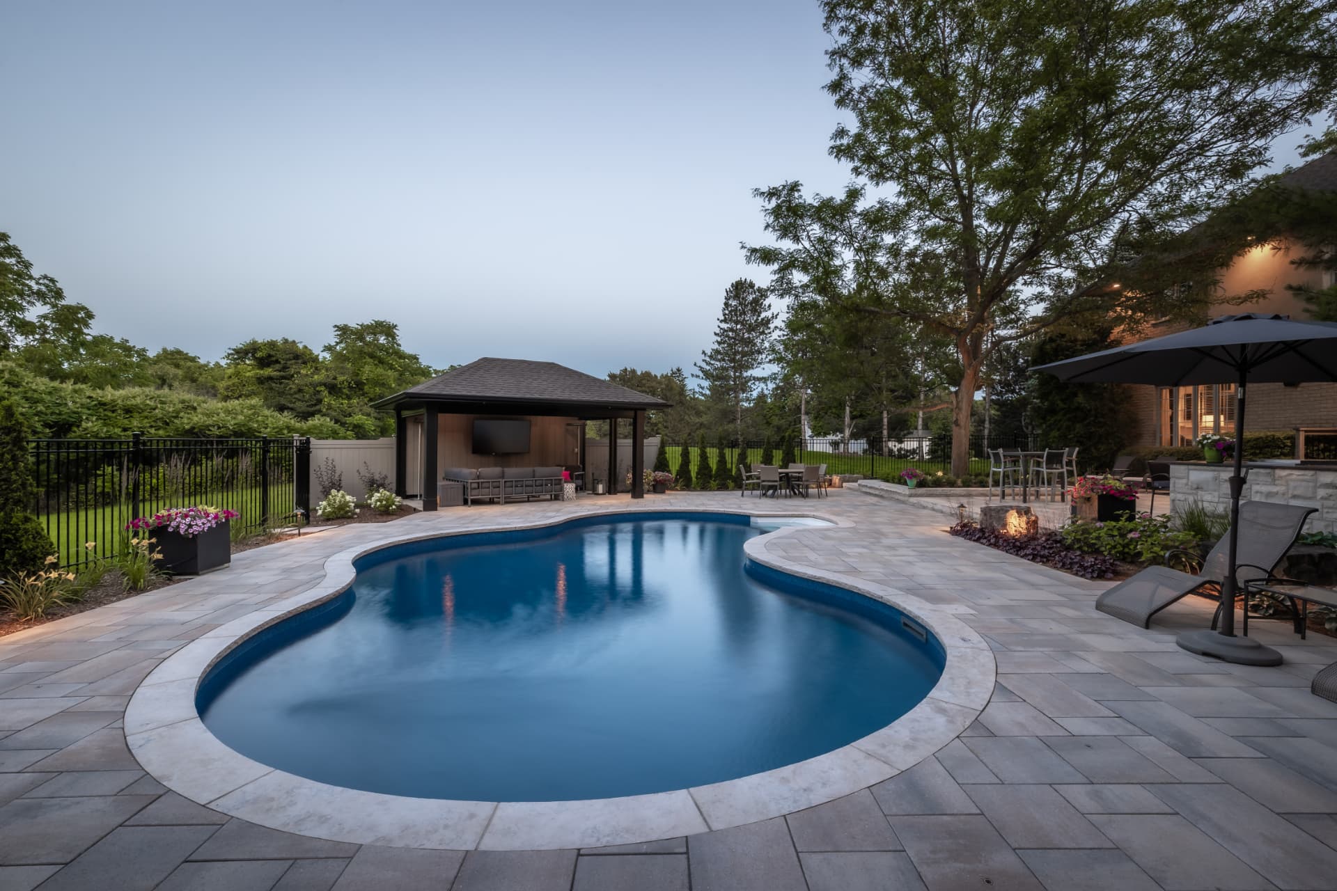 Freeform pool with paver deck and covered cabana lounge